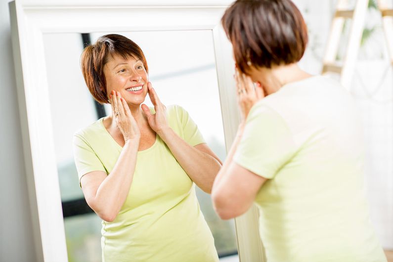 Mature woman looking in mirror after her Stem cell treatment.