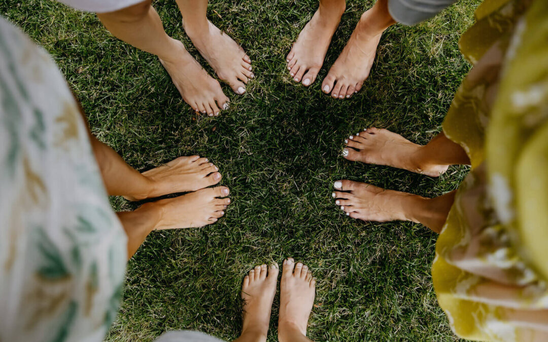 Five barefoot women stand in a circle on the grass